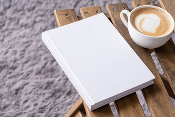 blank book mockup on wooden chair with cappuccino, pen and grey rug