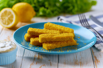 Tasty crispy deep fried fish fingers served with lemon and tartar sauce on wooden table.