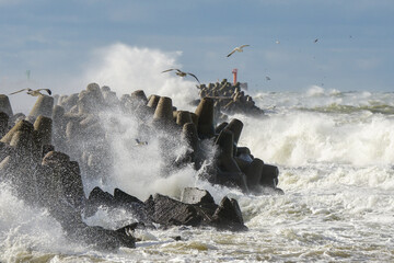 Storm at sea, high waves crashing against the concrete breakwaters of the port, high white splashes
