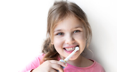 Beautiful blond girl cleaning her teeth with electric toothbrush on white background.Dental portrait.Smiling happy toddler.