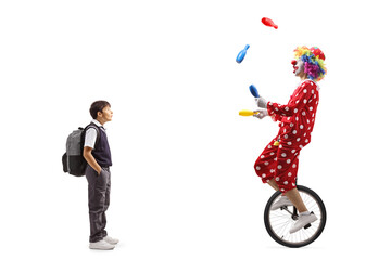 Full length shot of a surprised schoolboy looking at a clown juggling and riding a unicycle