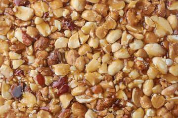 sweet peanut brittle close-up, vegetarian healthy sweet peanut in caramel snack treat with nutty flavor crumbly texture, full frame food background backdrop