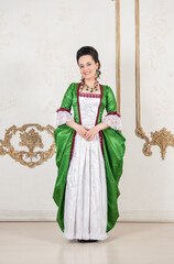 Beautiful woman in green rococo style medieval dress standing near wall