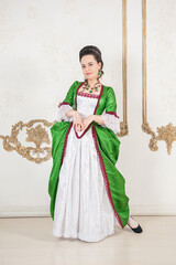 Beautiful smiling woman in green rococo style medieval dress standing near wall