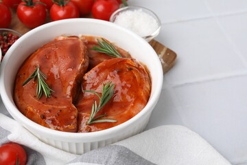Raw marinated meat and rosemary in bowl on white tiled table, closeup. Space for text