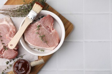 Raw meat, thyme, basting brush and marinade on white tiled table, top view. Space for text