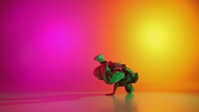 Talented man dressed sportswear and dancing solo in motion in neon light against gradient pink-yellow background. Concept of hobby, sport, creativity, fashion and style, motion, action. Ad