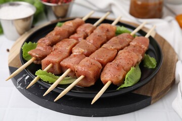 Wooden skewers with cut raw marinated meat on white tiled table, closeup