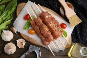 Skewers with cut raw marinated meat on wooden table, flat lay