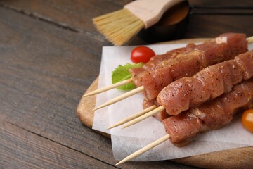 Skewers with cut raw marinated meat on wooden table. Space for text