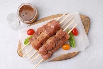 Wooden skewers with cut raw marinated meat on light grey table, flat lay