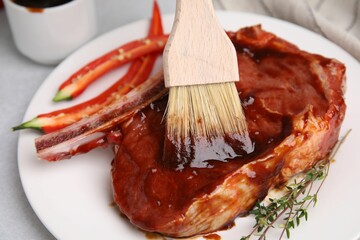 Spreading marinade onto raw meat with basting brush on table, closeup