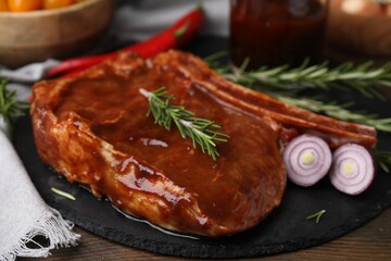 Tasty marinated meat, rosemary and onion on wooden table, closeup