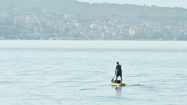 Unrecognizable person stand-up paddle boarding at Adriatic sea Kvarner gulf seen from the Crikvenica town coastline