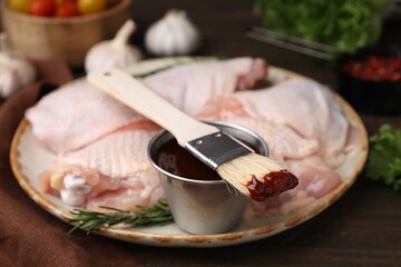 Plate with fresh marinade, raw chicken and basting brush on wooden table, closeup