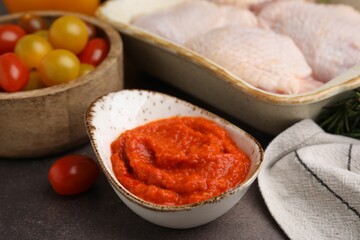 Fresh marinade, raw chicken and tomatoes on brown table, closeup