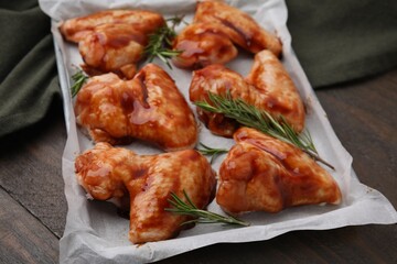 Raw marinated chicken wings and rosemary on wooden table, closeup
