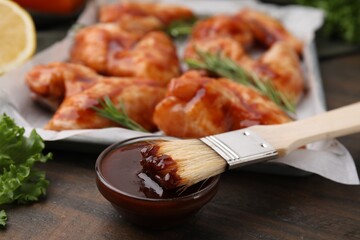 Fresh marinade, basting brush and raw marinated chicken wings on wooden table, closeup