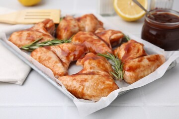 Raw marinated chicken wings and rosemary on light tiled table, closeup