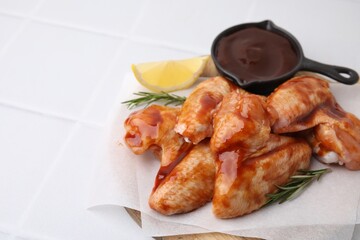 Raw chicken wings, rosemary, lemon and marinade on light tiled table, closeup. Space for text