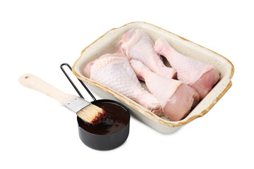 Raw chicken drumsticks in baking dish, marinade and basting brush isolated on white
