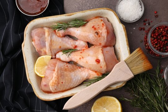 Flat lay composition with marinade and raw chicken drumsticks on brown table