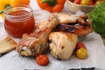 Marinade, basting brush, roasted chicken drumsticks and tomatoes on table, closeup