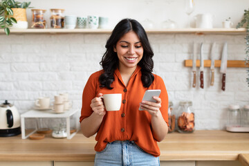 Cheerful woman using phone with coffee at home