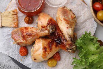 Marinade, basting brush, roasted chicken drumsticks, tomatoes and lettuce on table, flat lay