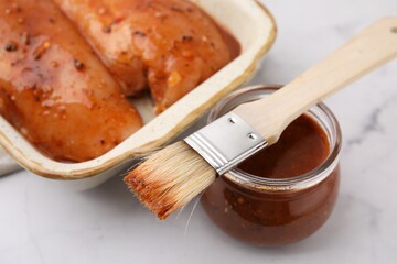 Fresh marinade, basting brush and raw chicken fillets on white table, closeup