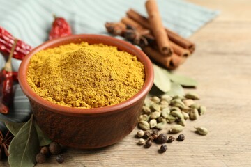 Curry powder in bowl and other spices on wooden table, closeup. Space for text