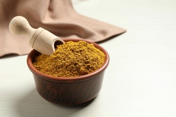 Curry powder in bowl and scoop on white wooden table, space for text