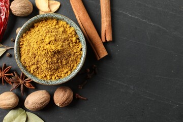 Dry curry powder in bowl and other spices on dark textured table, flat lay. Space for text