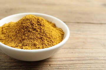 Dry curry powder in bowl on wooden table, closeup. Space for text