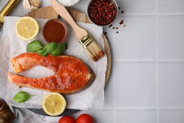 Fresh marinade, fish, lemon, brush and basil on white tiled table, flat lay. Space for text