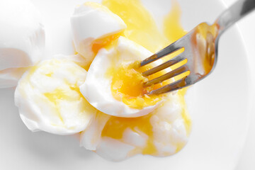 Poached eggs with with egg yolk and a fork on a white plate. 