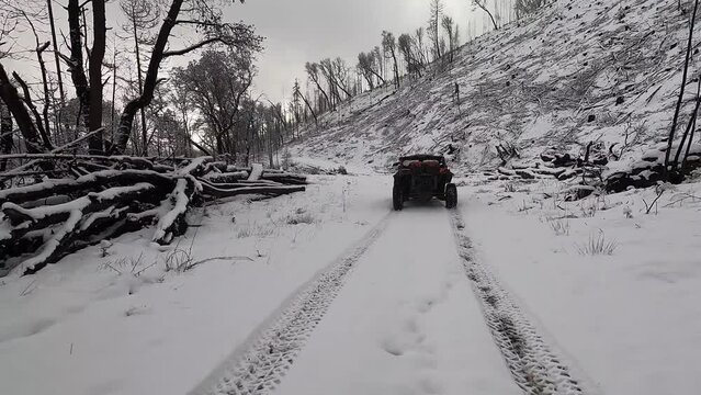 A red ATV is parked in the snow on a road. The snow is deep and the sky is cloudy