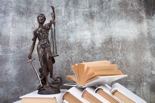 Law concept - Open law book, Judge's gavel, scales, Themis statue on table in a courtroom or law enforcement office. Wooden table, gray concrete background.