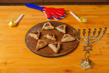 Sweet gomentashi cookies on a wooden board next to a clapper and a menorah for the holiday of Purim
