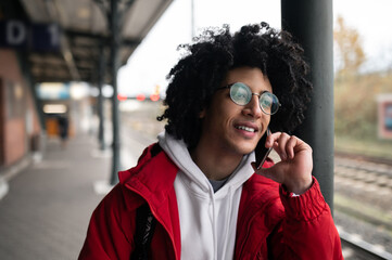 Curly-haired guy in eyeglasses with a phone in hands at the railway platform
