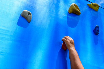 Young woman hand holding hook at the blue climbing wall