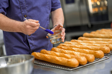 Unrecognizable man baker baking baguettes in bakehouse