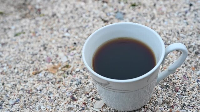 Cup full of coffee in a porcelain cup on the sand at the beach