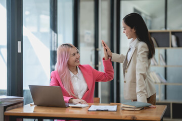 Two businesswomen celebrating their success with a high five in the office.