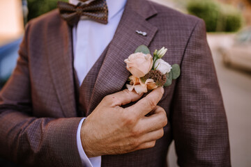 Valmiera, Latvia- July 28, 2024 - A close-up of a man in a suit adjusting a floral boutonniere on his lapel, with a patterned bow tie, representing classic wedding attire and preparation.