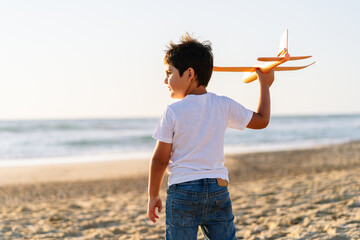 A child poised to send a plane soaring beside the sea