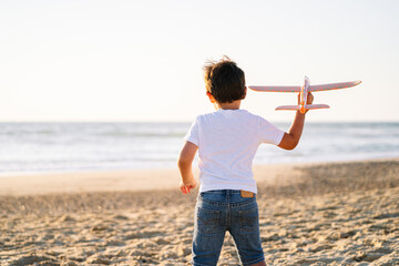 Back view of a young boy with a toy airplane at the beach.
