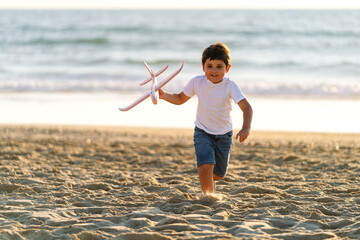 Excited boy plays with a plane on sandy beach during sunset.