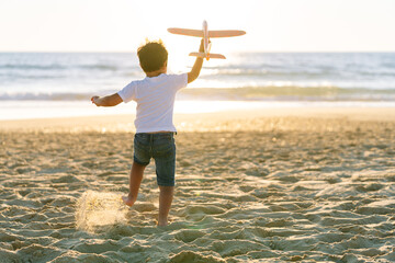 A child runs on the beach, airplane in hand, ready to fly.