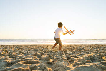 A boy runs with a toy plane against a sunset